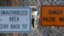 A Pennsylvania prison staffer walks in an area surrounded by fencing, barbed wire, and warning signs.